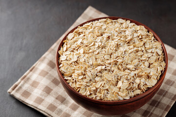 Oat flakes in bowl on a linen napkin. Raw oatmeal on a dark background. Vegan food concept