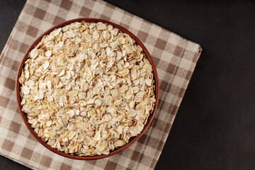 Oat flakes in bowl on a linen napkin. Raw oatmeal on a dark background. Vegan food concept