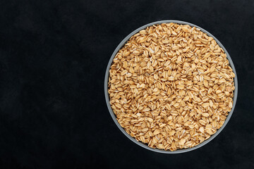 Oat flakes in a bowl on a dark background. Uncooked rolled oats for a healthy diet. Gluten free diet concept. Copy space