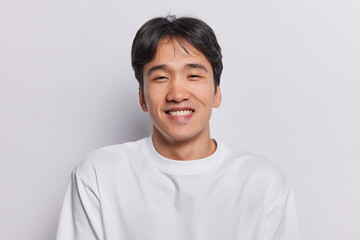 Portrait of handsome cheerful Japanese man smiles toothily being in good mood enjoys day off vacation dressed in casual t shirt isolated over white background. People ethnicity and emotions concept