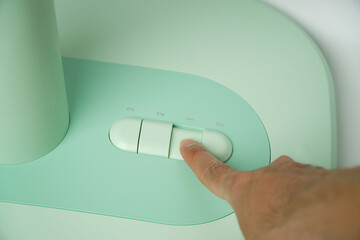 Hand presses the button on the control panel on the green electric fan
