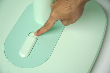 Hand presses the button on the control panel on the green electric fan