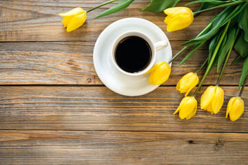 Fototapeta na wymiar Bouquet of yellow tulips and cup of coffee on a wooden background, top view.