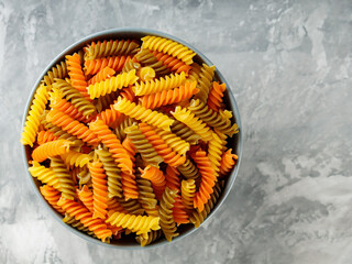 Fusilli pasta with spinach and tomato on a gray background. Raw colorful italian fusilli pasta in a bowl. Top view. Copy space
