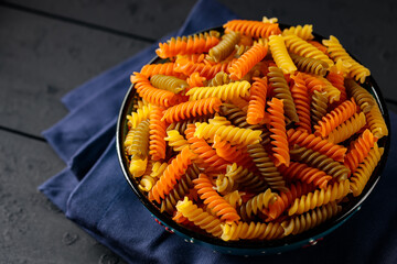 Raw fusilli pasta in bowl on dark wooden background. Tricolor fusilli pasta on a blue linen napkin....