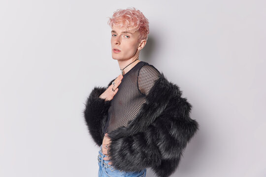 Sideways shot of seductive handsome pink haired man dressed in fashionable clothes looks seriously at camera isolated over white background. Non binary person. Gender transformation concept.