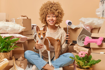 Cheerful woman poses with favorite pet holds paint roller moves to new apartment going to make...