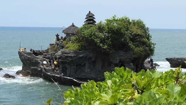Pura Tanah Lot temple in Bali, Indonesia surrounded by water. Iconic Balinese water temple on a sunny day. Religious landmark of Bali. Bali sightseeing highlights. Beautiful old building on a rock. 