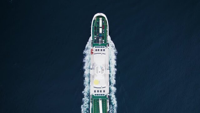 Top down aerial drone view on transportation logistics ferry cruise move through deep blue water with passengers and vehicles on board