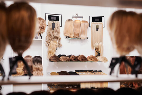 Showcase of natural looking wigs in different colors fixed on the metal wig holders in beauty salon. Row of mannequin heads with variation shades hair on shelf in wig shop.