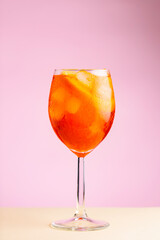 Glass of Aperol Spritz cocktail on a pink beige background. Cocktail Aperol Spritz with orange and ice cubes. Summer refreshing drink concept