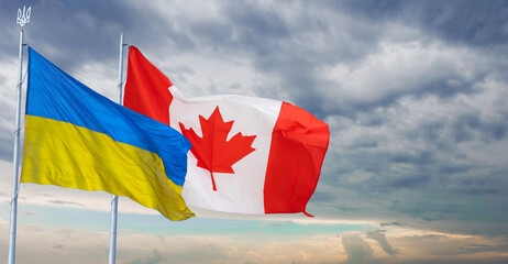 Ukraine and Canada two flags on flagpoles and blue sky.
