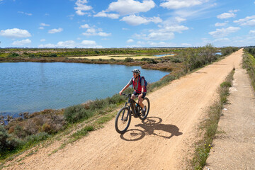Fototapeta na wymiar beautiful senior woman cycling with her electric mountain bike on a via verde in the wetlands of Isla Christina, Andalusia, Spain