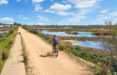 beautiful senior woman cycling with her electric mountain bike on a via verde in the wetlands  of Isla Christina, Andalusia, Spain