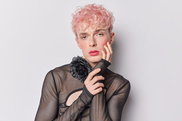 Horizontal shot of serious gay with dyed pink hair has rouge cheeks vivid makeup keeps hand on...