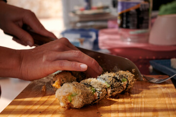 A person is preparing a homemade Japanese sushi meal, cutting fresh rolls on the board with a sharp knife.