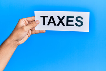 Hand of caucasian man holding paper with taxes word over isolated blue background