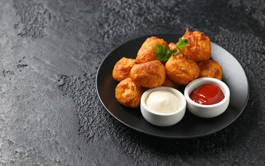 Battered chicken balls with tomato ketchup, mayonnaise on black plate. Party food