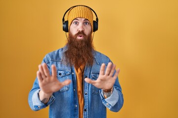Caucasian man with long beard listening to music using headphones moving away hands palms showing...