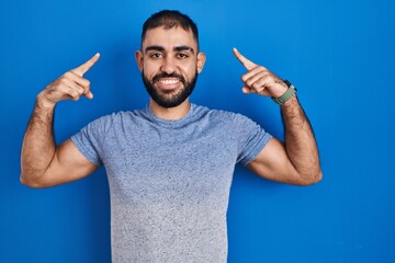 Middle east man with beard standing over blue background smiling pointing to head with both hands finger, great idea or thought, good memory