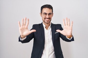 Handsome business hispanic man standing over white background showing and pointing up with fingers number ten while smiling confident and happy.