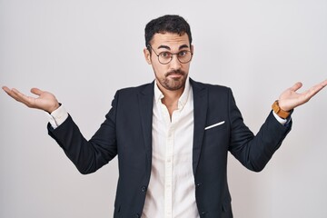 Handsome business hispanic man standing over white background clueless and confused expression with arms and hands raised. doubt concept.