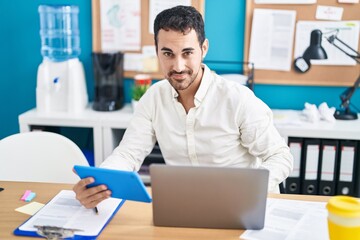 Obraz premium Young hispanic man business worker using laptop and touchpad working at office