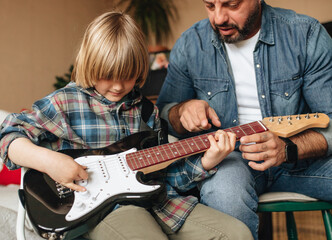 father teaching son to play guitar