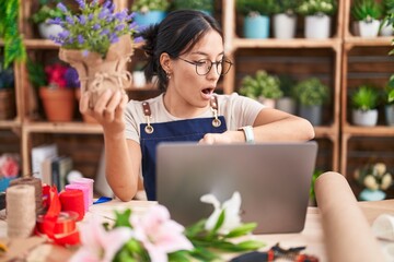 Young hispanic woman working at florist shop doing video call looking at the watch time worried,...