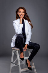Full length studio shot of a brunette haired beautiful woman sitting at grey background