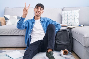 Young hispanic man sitting on the floor studying for university smiling looking to the camera...