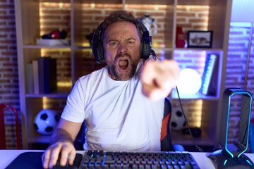 Middle age man with beard playing video games wearing headphones pointing displeased and frustrated to the camera, angry and furious with you