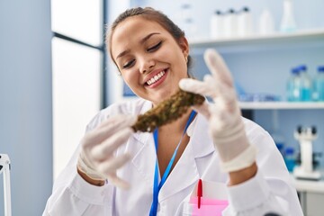 Young beautiful hispanic woman scientist smiling confident holding marijuana at laboratory