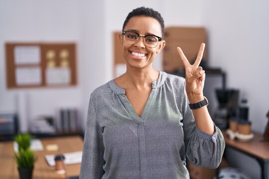 African american woman working at the office wearing glasses showing and pointing up with fingers number two while smiling confident and happy.