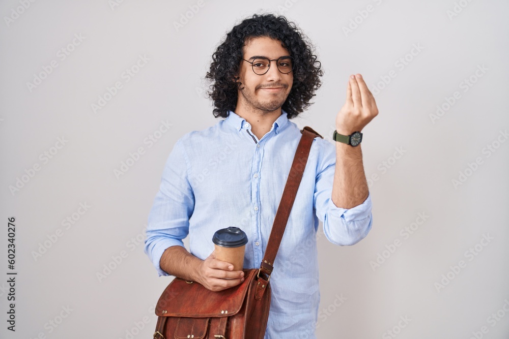 Wall mural Hispanic man with curly hair drinking a cup of take away coffee doing italian gesture with hand and fingers confident expression