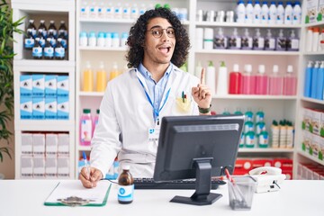 Hispanic man with curly hair working at pharmacy drugstore pointing finger up with successful idea. exited and happy. number one.