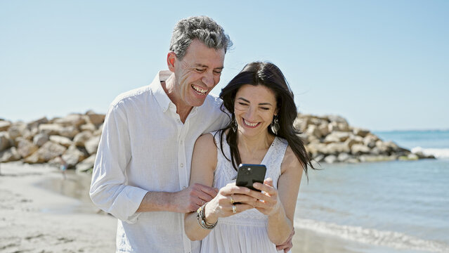 Senior man and woman couple smiling confident using smartphone at seaside
