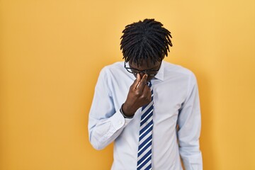 African man with dreadlocks standing over yellow background tired rubbing nose and eyes feeling fatigue and headache. stress and frustration concept.