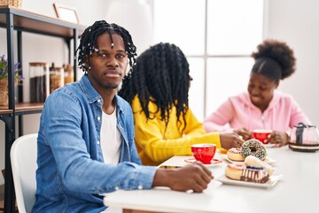 Fototapeta na wymiar Group of three young black people sitting on a table having coffee thinking attitude and sober expression looking self confident