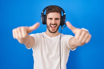 Naklejka premium Hispanic man with beard listening to music wearing headphones approving doing positive gesture with hand, thumbs up smiling and happy for success. winner gesture.