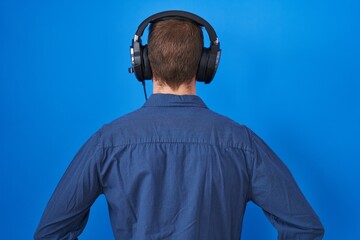 Hispanic man with beard listening to music wearing headphones standing backwards looking away with...