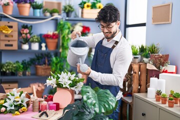 Young hispanic man florist smiling confident watering flowers at florist shop