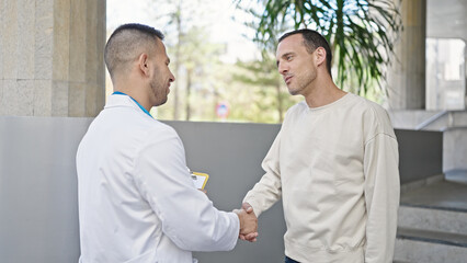 Fototapeta na wymiar Two men doctor and patient having medical consultation shake hands at hospital