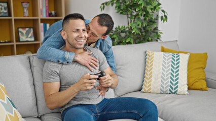 Two men couple playing video game hugging each other at home