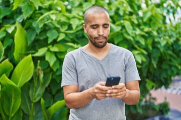 Naklejka na ściany i meble Young latin man using smartphone with serious expression at park