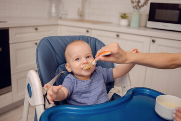A beautiful baby eating mashed potatoes. Mom feeds baby.