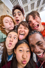 Vertical multi-ethnic group of crazy students boys and girls taking selfie outdoors. Young people enjoying making comical face gestures to upload funny photo to social networks. 