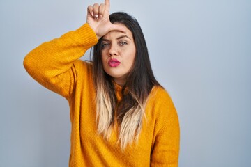 Young hispanic woman standing over isolated background making fun of people with fingers on...