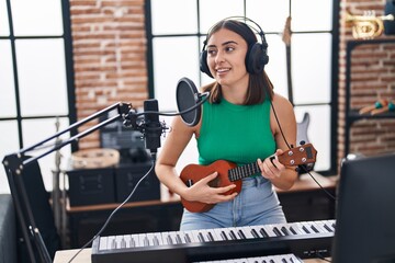 Young hispanic woman musician singing song playing ukelele at music studio