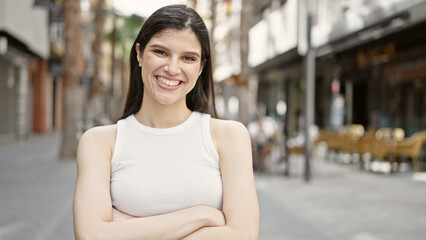 Young beautiful hispanic woman standing with crossed arms at street